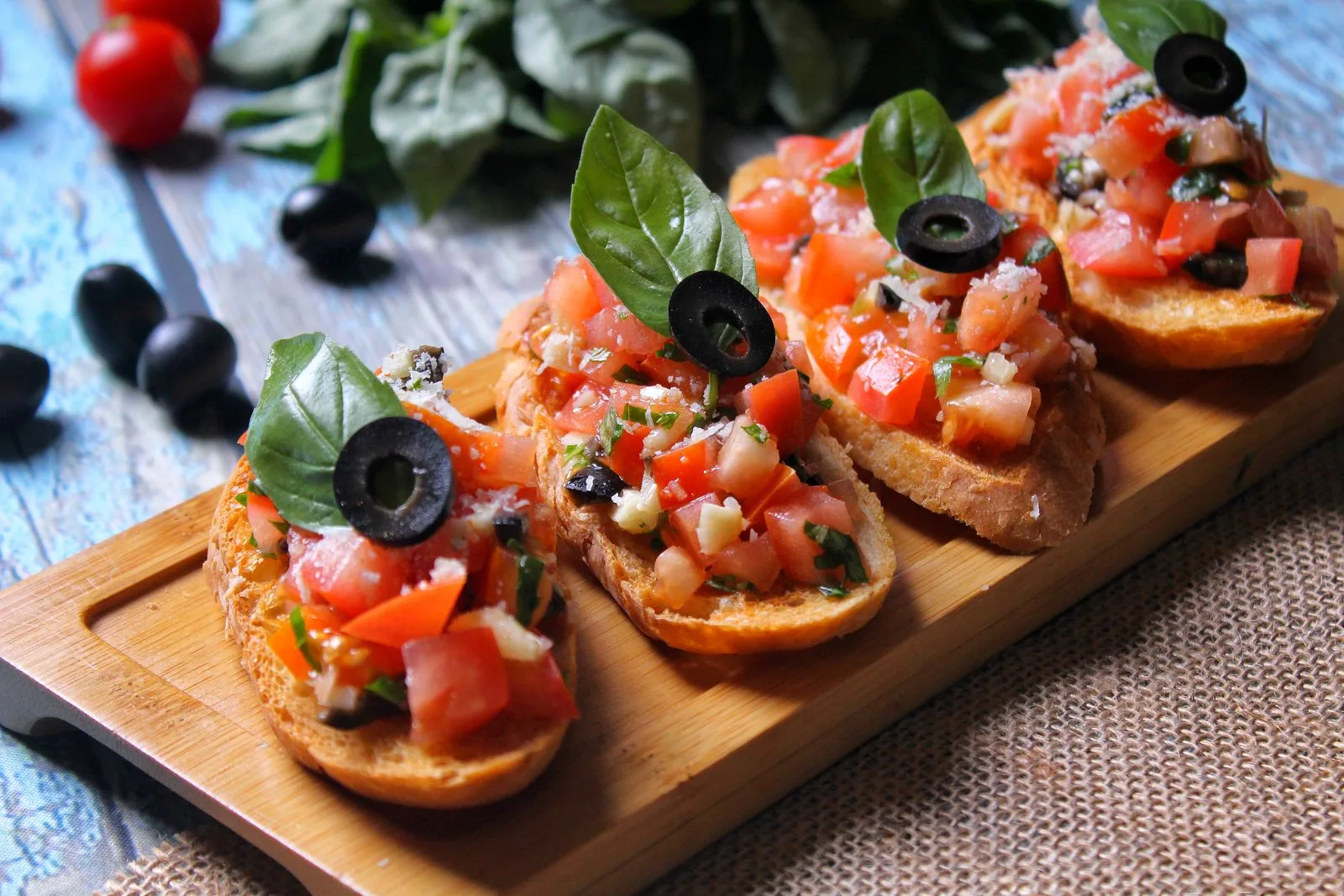 Three slices of bruschetta with tomatoes, black olives and basil on a wooden board