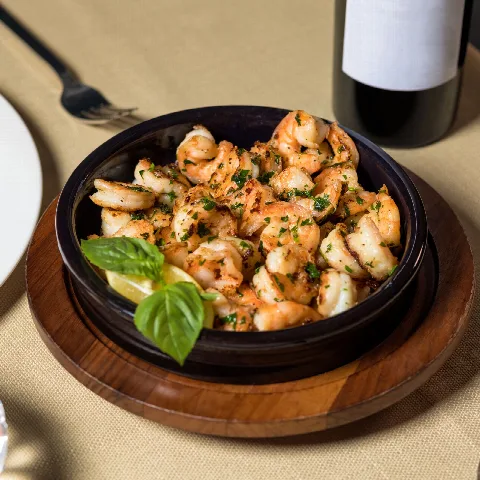 Garlic prawns sizzling in a dark skillet with lemon and basil