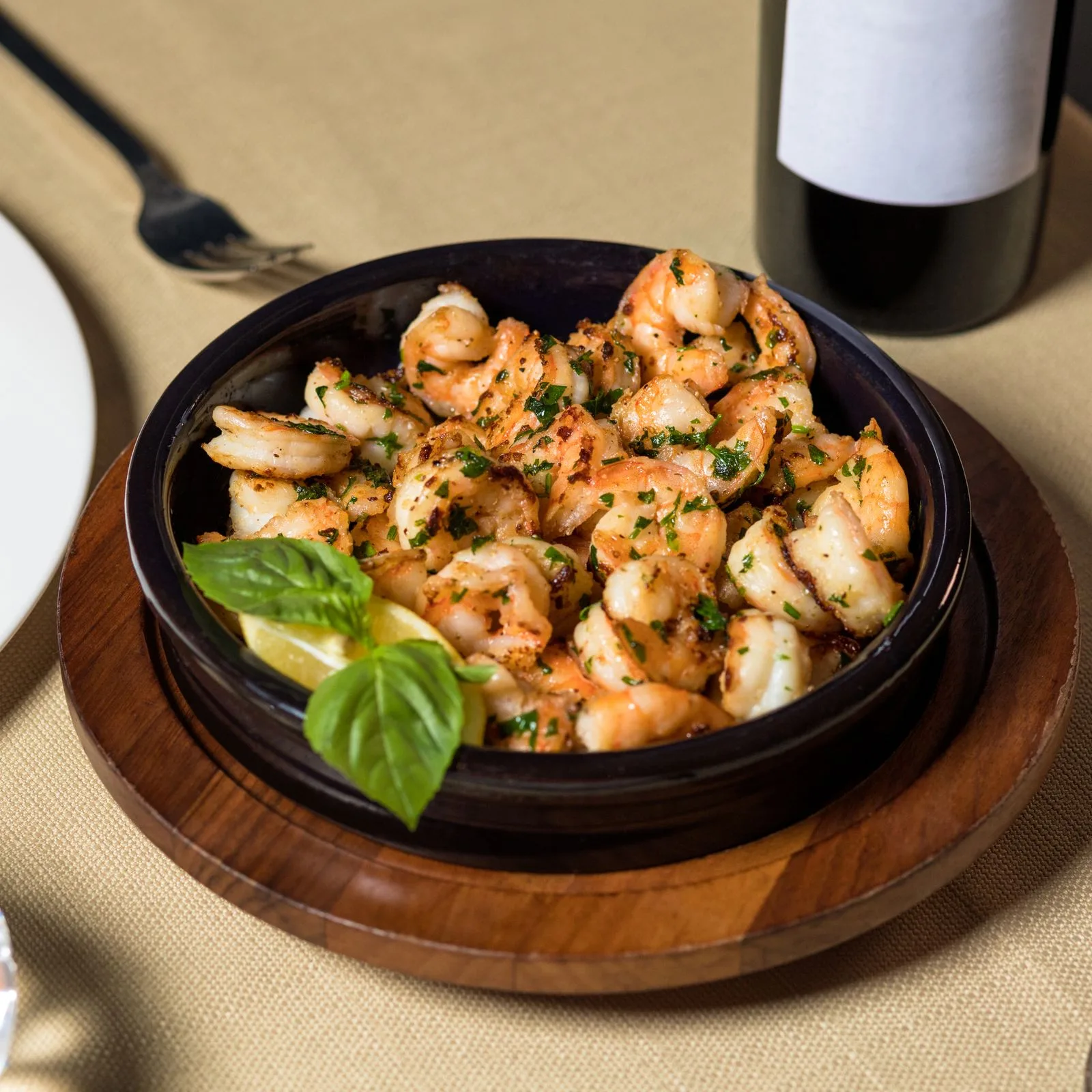 Garlic prawns sizzling in a dark skillet with lemon and basil