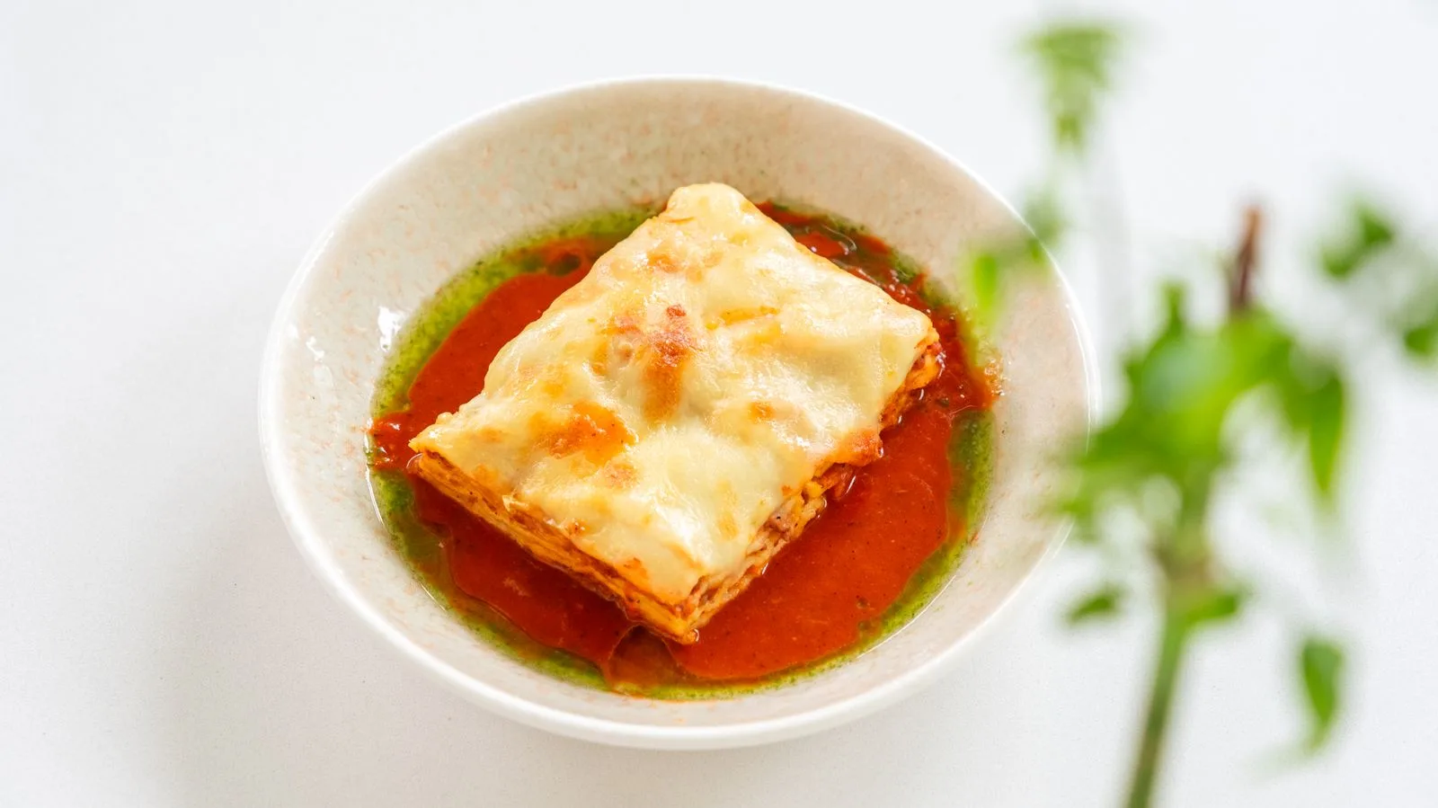 A square of baked lasagna in a bowl with tomato sauce