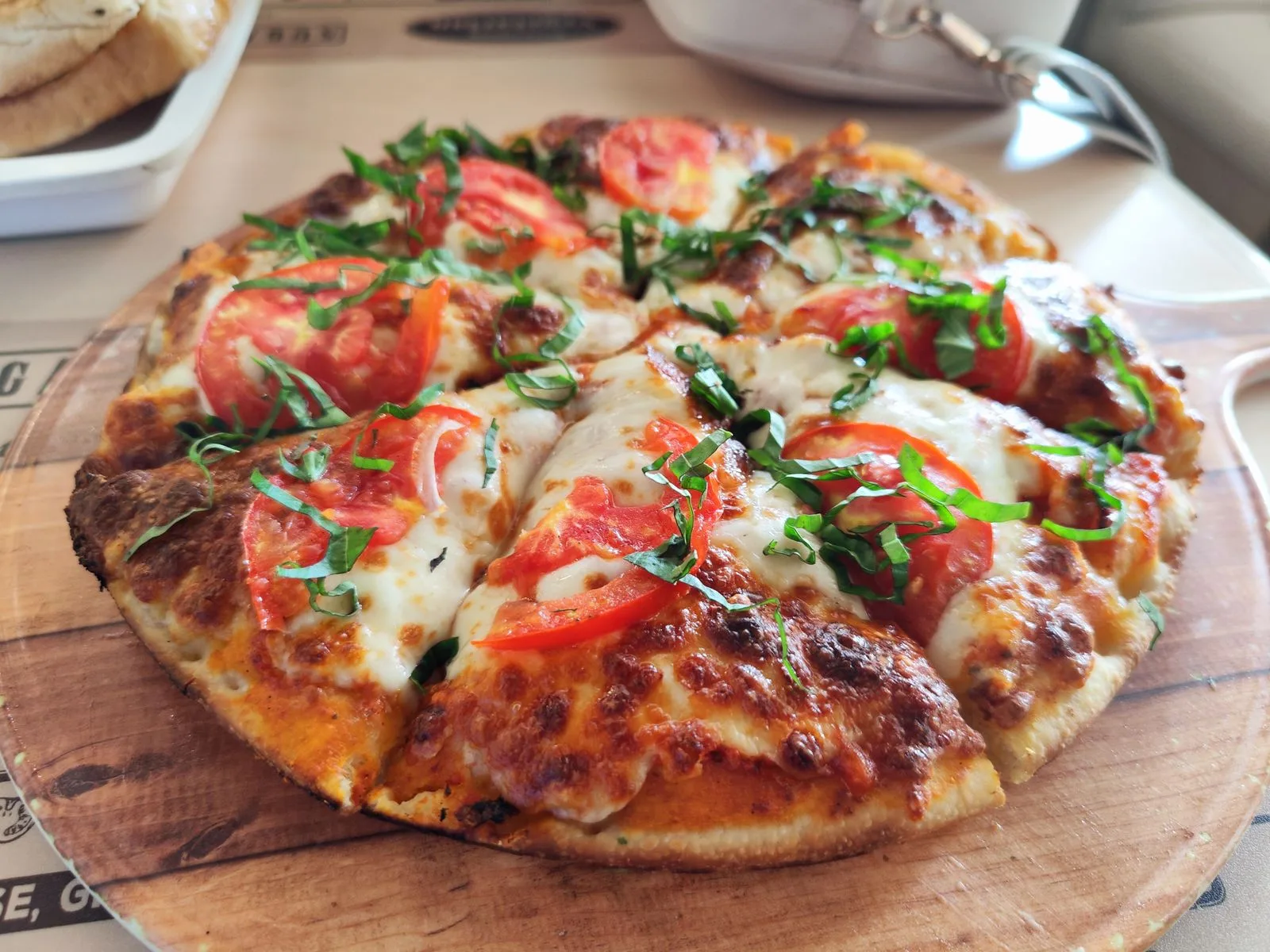 Margherita pizza with tomato slices and basil on a wooden board